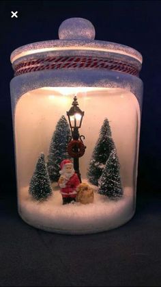 a glass jar filled with snow covered trees and a santa clause figurine in it