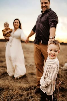 a little boy standing in the middle of a field with his parents