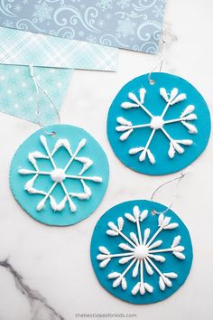 three snowflake ornaments are hanging on a marble countertop, one is blue and the other is white