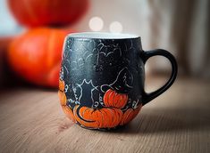 a black coffee mug decorated with cats and pumpkins on a table next to two orange pumpkins