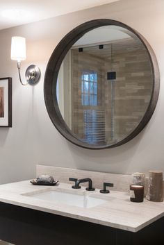 a bathroom sink under a round mirror in front of a wall mounted faucet