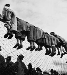 a group of people hanging upside down on a fence with their feet in the air