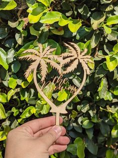 a hand holding a wooden cutout of two palm trees with the word love in it