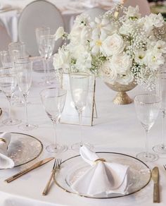 the table is set with white flowers and silverware