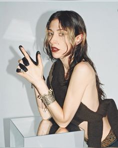 a woman with black nails holding her hand up in the air while sitting on a white surface