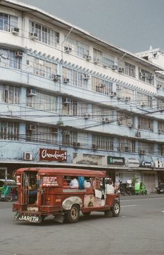 an old red bus driving down the street in front of a tall building with many windows