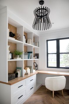 an office with white bookcases and wooden flooring next to a large window