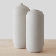 two white vases sitting on top of a wooden table