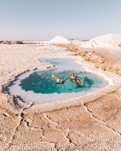 two people swimming in the dead sea with white sand and clear blue water on either side