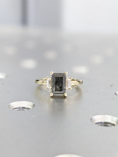 an engagement ring with a black diamond surrounded by smaller white diamonds on a metal surface