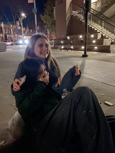 a woman sitting on the ground with her arm around another woman's shoulder and smiling