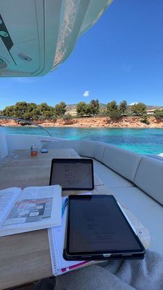 two ipads are sitting on a table in front of the ocean and an open book