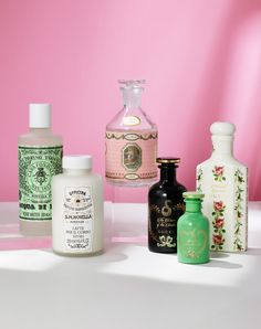 several different types of perfume bottles on a table against a pink background with white shadows