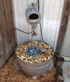 a water fountain made out of an old barrel filled with rocks and pebbles is shown in front of a wooden fence