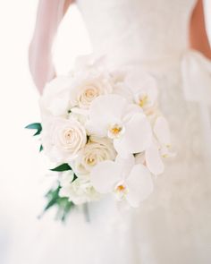 a bride holding a bouquet of white roses and orchids on her wedding day,