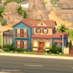 a blue and tan house with palm trees on the side of the road in front of some mountains