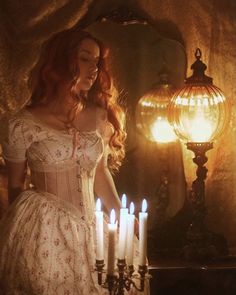 a woman in a white dress standing next to a bunch of candles on a table