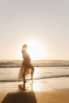 a woman standing on top of a sandy beach next to the ocean at sun set