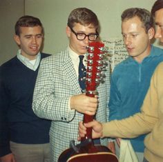 three men standing next to each other with a guitar in front of them and one man holding an instrument