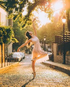 a woman in a white dress is dancing on a cobblestone street at sunset