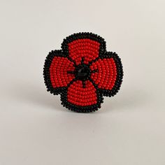 a red and black beaded brooch sitting on top of a white surface