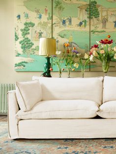 a white couch sitting in front of a wall with paintings on it's walls