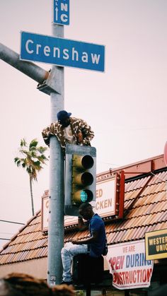 a man sitting on top of a traffic light next to a street sign