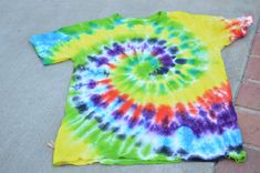 a tie - dyed t - shirt laying on the ground next to a brick wall