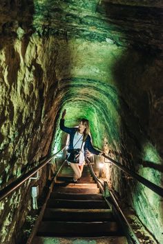 a woman is walking up some stairs in a tunnel with green light coming from the ceiling