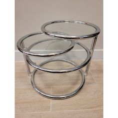 three round glass tables with metal bases on the floor in front of a white wall