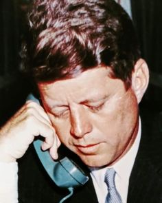 a man in a suit and tie talking on a cell phone while holding his hand to his ear