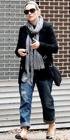 a woman in black jacket and scarf standing on sidewalk