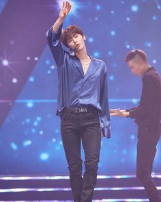 a male in a blue shirt and black pants is on stage with his hand up