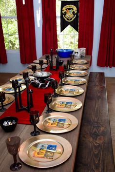 a long table with plates and candles on it in front of red drapes