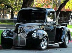 an old black car parked on the side of the road with a heart shaped tree in the background