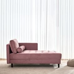 a pink couch sitting on top of a rug in front of a window with vertical blinds