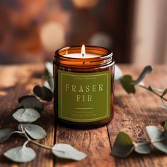 a candle sitting on top of a wooden table next to some leaves and greenery