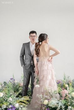 a man and woman standing next to each other in front of flowers