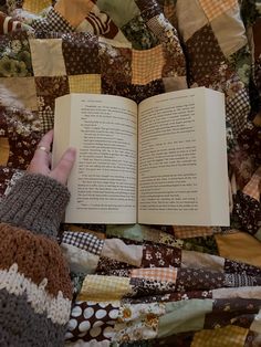 a person is reading a book on top of a bed covered in patchwork material