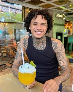 a man sitting at a table with a drink in his hand and tattoos on his arm