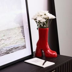 A bright red boot-shaped vase with a collection of white flowers inside. The vase is on a table with a notebook and pen beside it. Red Accent Aesthetic, Red Dorm Decor, Pink And Red Room Aesthetic, Red Room Decor Aesthetic, Red Accent Decor, Red Apartment Decor, Arty Bedroom, Vintage Room Aesthetic, Red Dorm