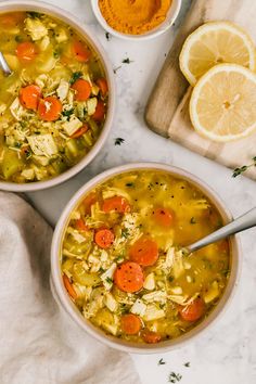 two bowls filled with chicken soup next to some sliced lemons and carrots on a cutting board