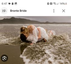 a man and woman kissing on the beach in front of an ocean with waves crashing over them