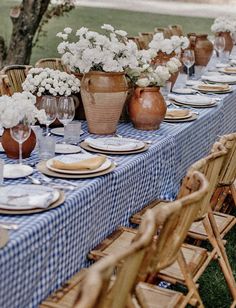 a table set with plates and vases filled with white flowers on top of a blue checkered table cloth