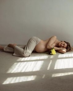 a naked woman laying on the floor next to a vase with yellow flowers in it