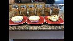 three red plates topped with food on top of a counter next to jars filled with food