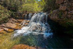 there is a waterfall in the middle of some rocks and green trees on either side