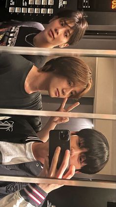 two young men standing next to each other in front of a mirror looking at their cell phones