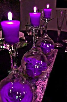 purple candles are sitting in wine glasses on a table