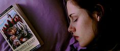 a woman laying in bed next to a book